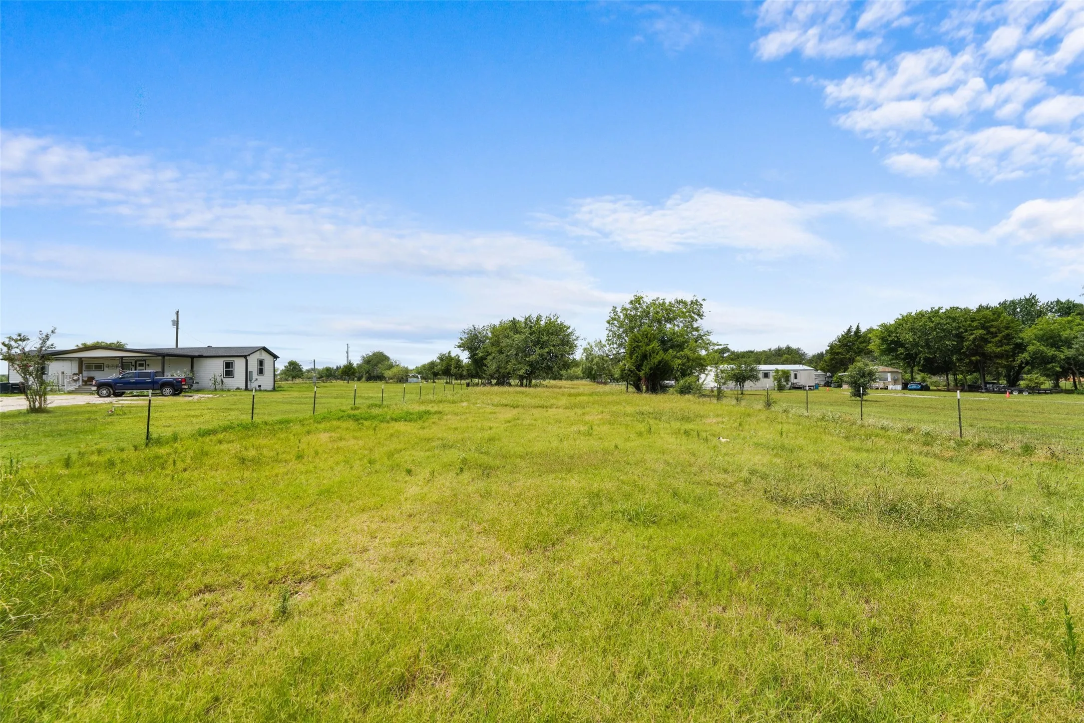 Expansive green field with partial fencing and surrounding mature trees