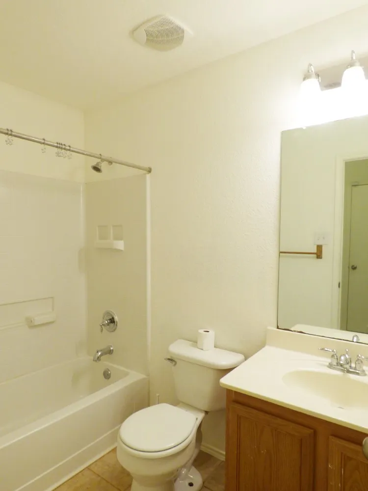 Bathroom featuring a white bathtub and shower combination, a white toilet, a wood-finish vanity with an integrated sink, a rectangular mirror, and tile flooring