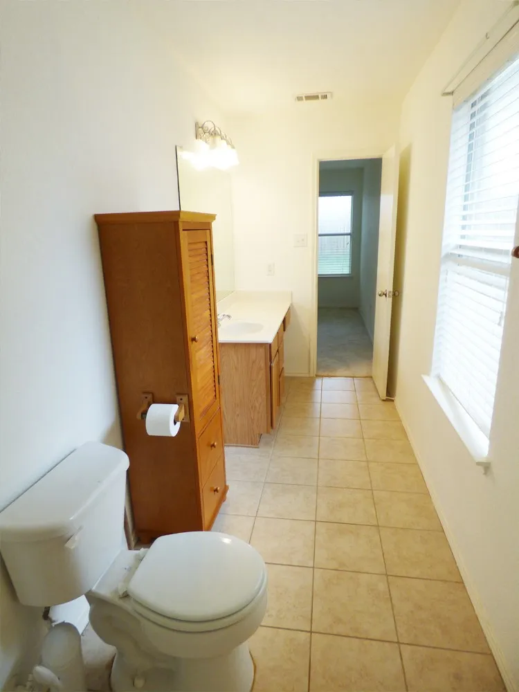Bathroom featuring a single vanity with laminate countertop, integrated sink, and wood-finish cabinetry
