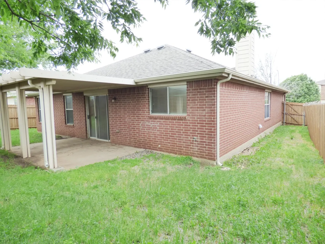 Brick exterior featuring a covered patio with concrete flooring, a sliding glass door, multiple windows with blinds, and a wooden fence