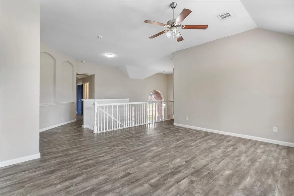 Spacious room featuring vaulted ceilings, wood-finish flooring, a contemporary ceiling fan, and a white balustrade overlooking a lower level