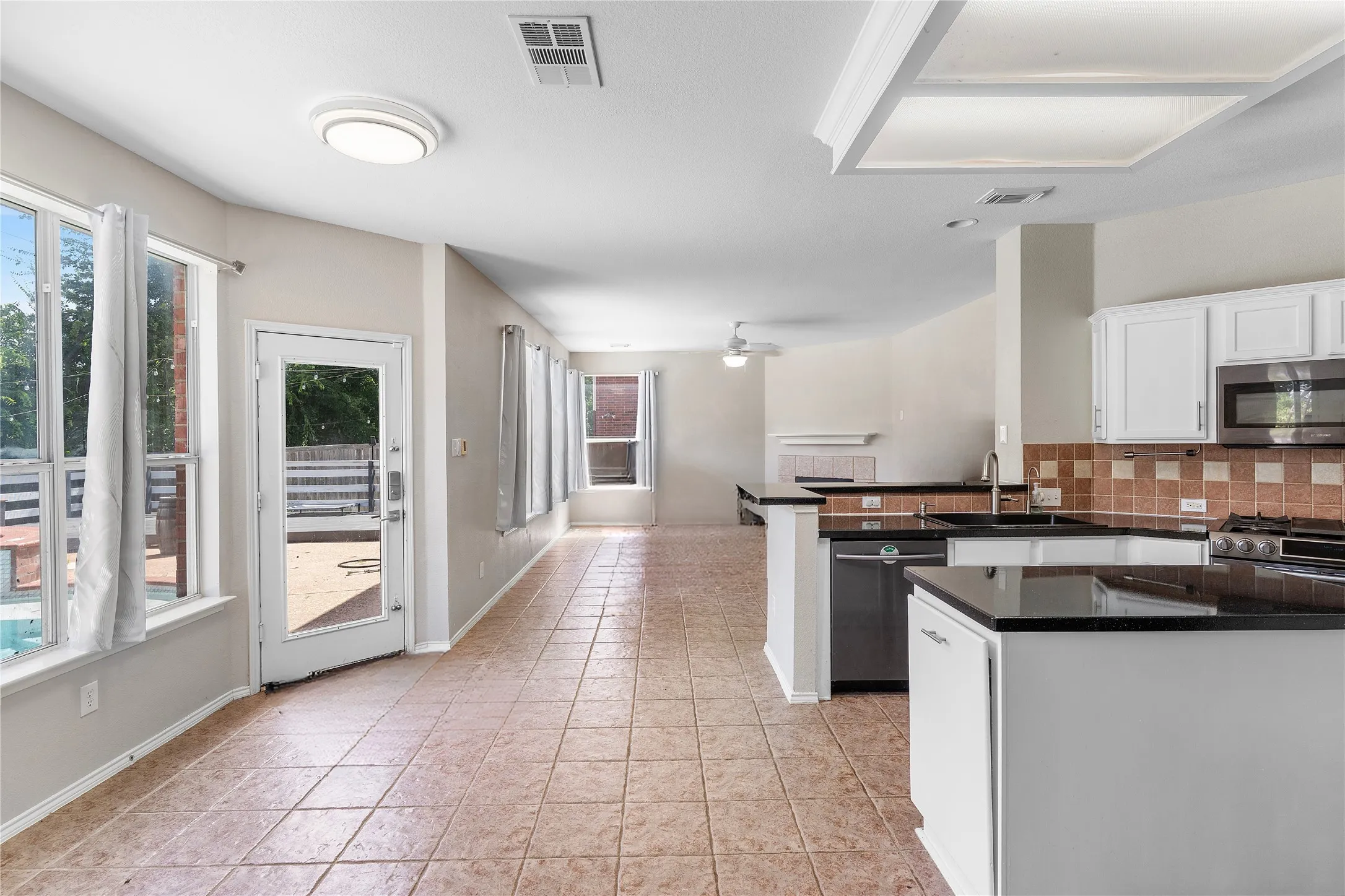 Spacious kitchen and dining area featuring white cabinetry, black granite countertops, stainless steel appliances, tile flooring, and abundant natural light from multiple windows and glass doors opening to an outdoor patio