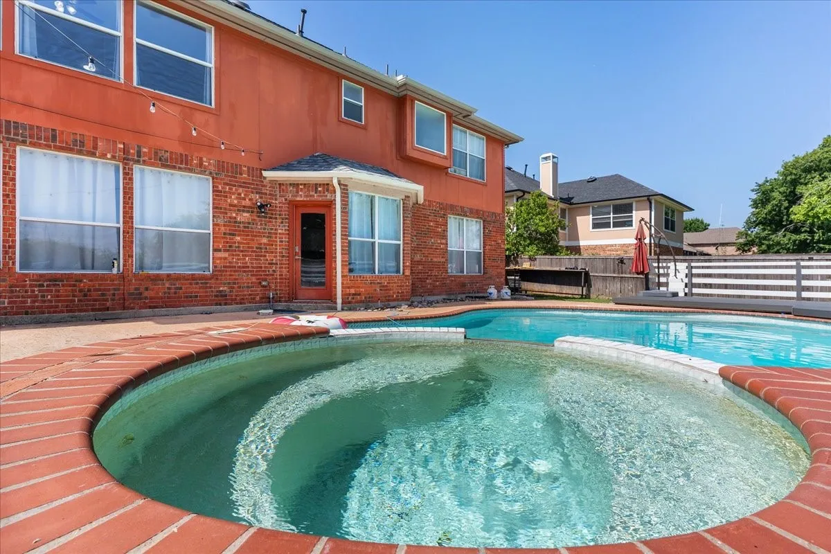 Outdoor living space featuring a brick-lined spa and swimming pool, surrounded by a concrete patio