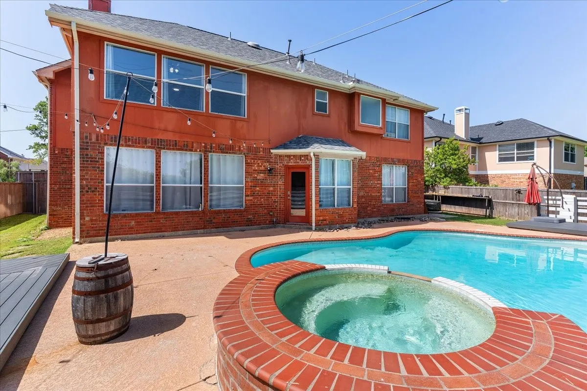 Spacious backyard featuring a freeform swimming pool and integrated hot tub with brick coping