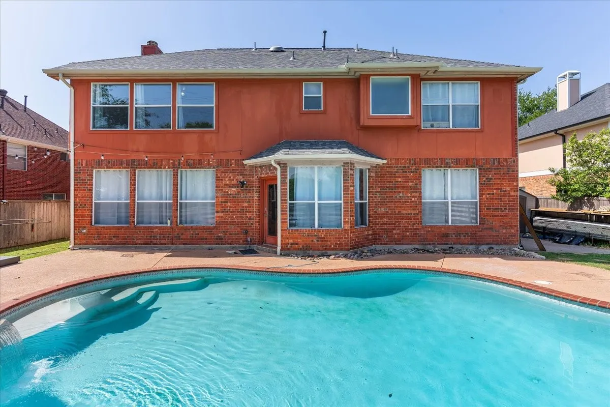 Curved swimming pool with concrete decking surrounds a two-story brick and stucco exterior
