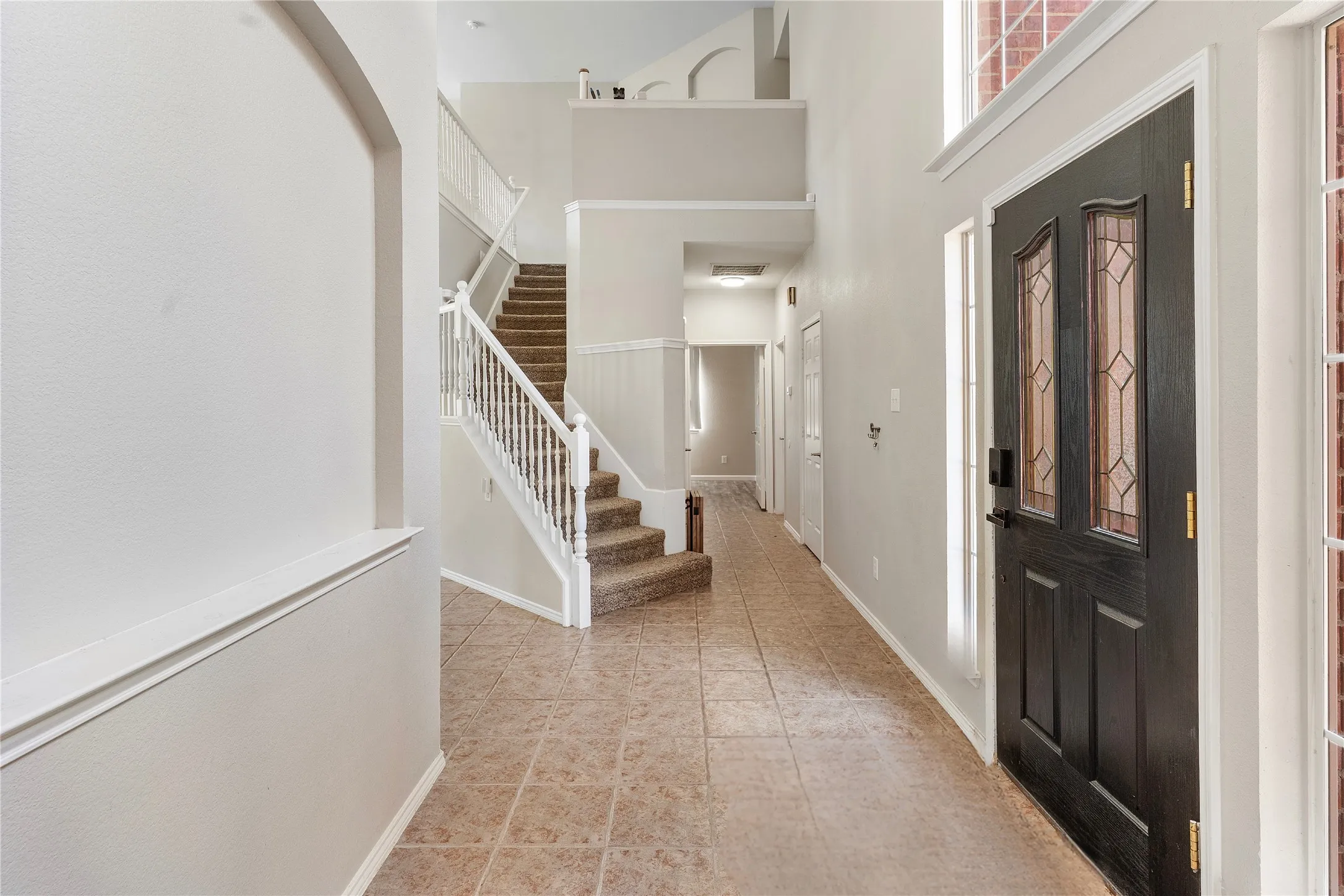 Entryway featuring a dark wood-finish door with decorative glass inserts, tile flooring, and a two-story ceiling