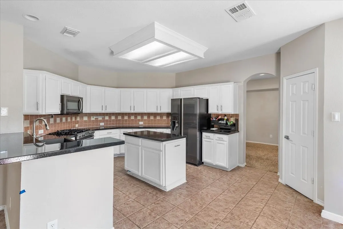 Kitchen featuring white cabinetry, a central island, dark countertops, and a tile backsplash