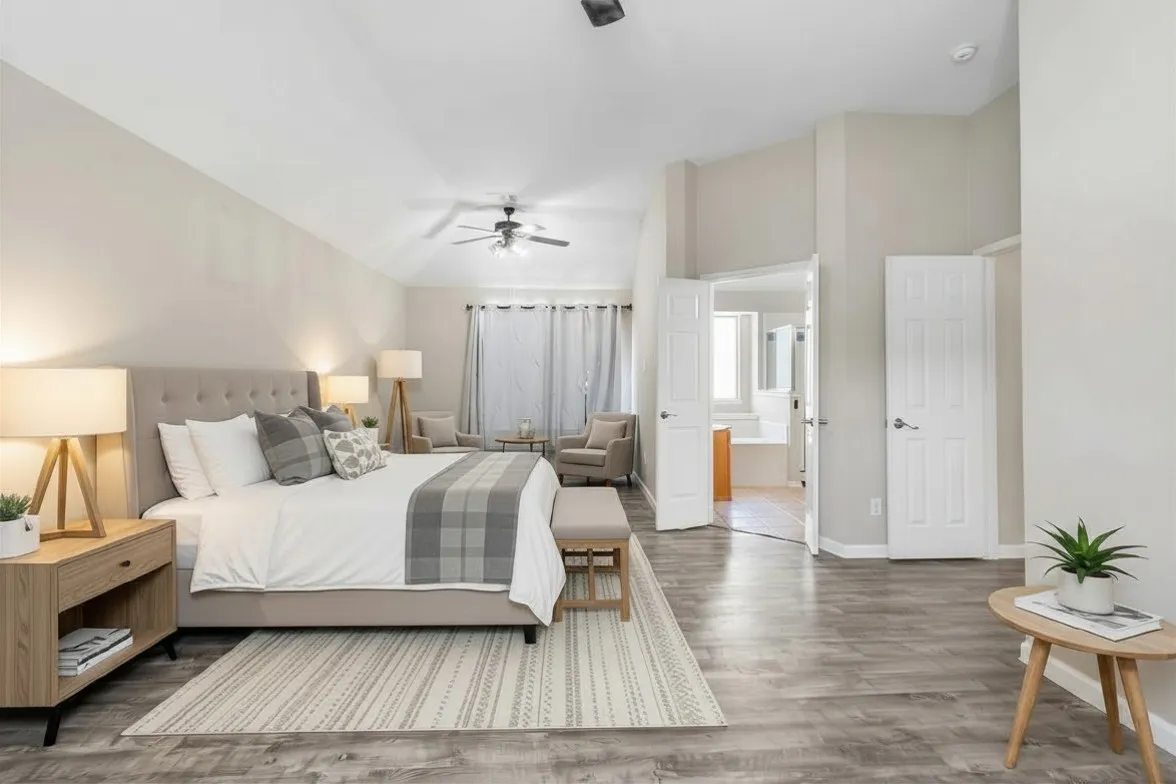 Spacious bedroom featuring wood-finish flooring, a ceiling fan with integrated lighting, and a recessed sitting area