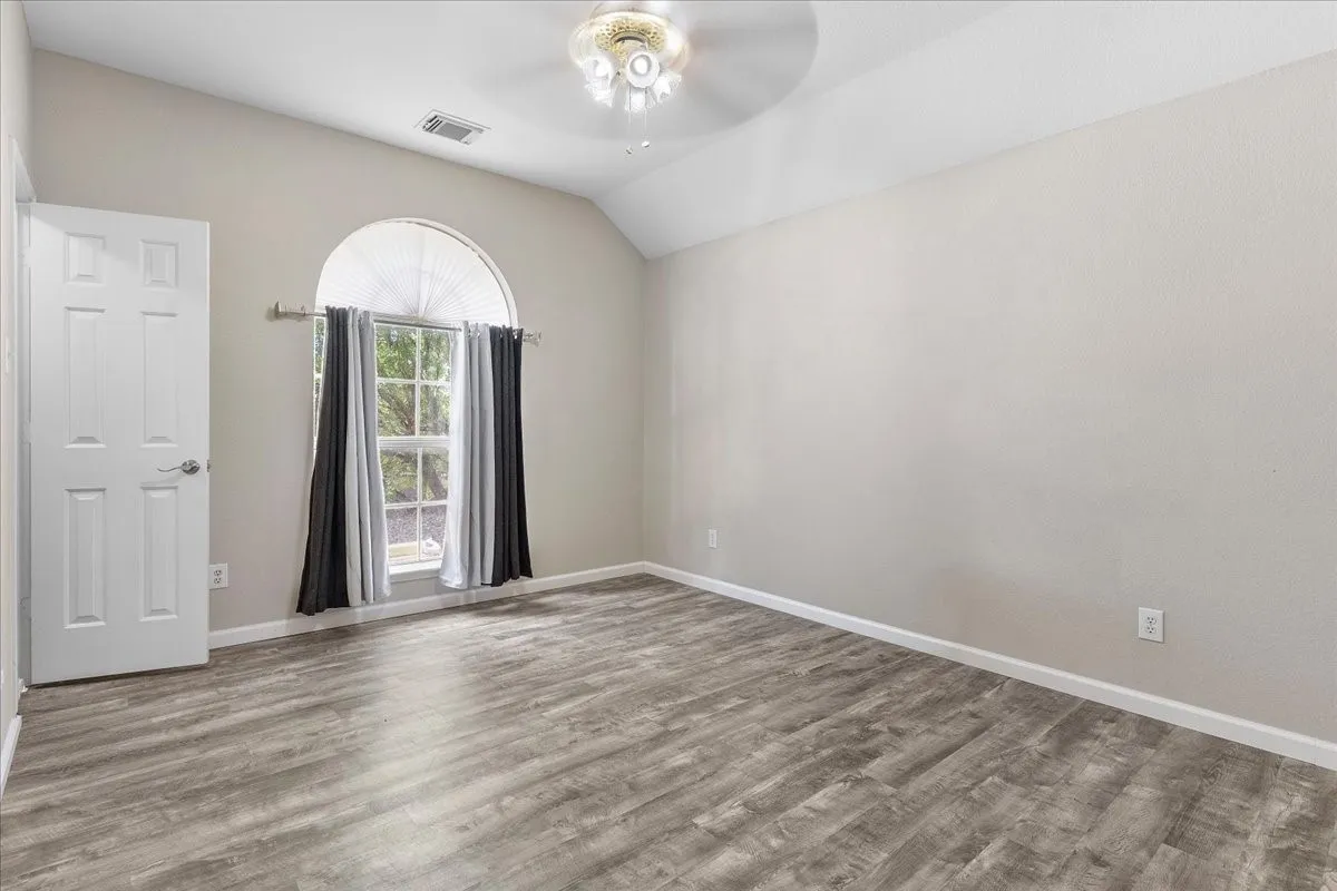 Spacious room featuring vaulted ceilings, wood-finish flooring, a large arched window, and a ceiling fan with integrated lighting