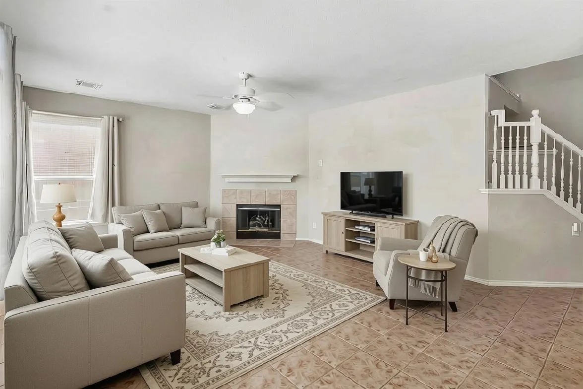 Living area featuring a tile-surround fireplace with a mantel, a ceiling fan with integrated lighting, and a white baluster staircase
