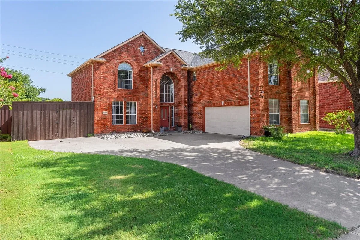 Red brick two-story residence featuring an arched entry, multiple window styles including arched and rectangular, an attached garage, and a concrete driveway