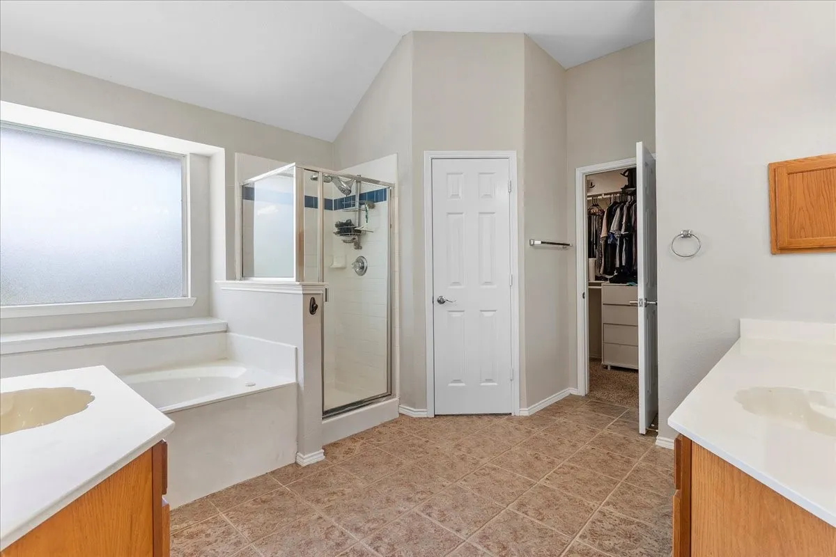 Bathroom featuring a separate shower enclosure with glass surround, a built-in soaking tub, and dual vanity areas with wood cabinetry