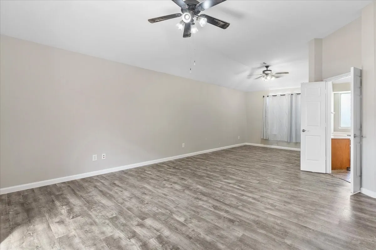 Spacious room featuring vaulted ceilings, wood-finish flooring, and multiple ceiling fans