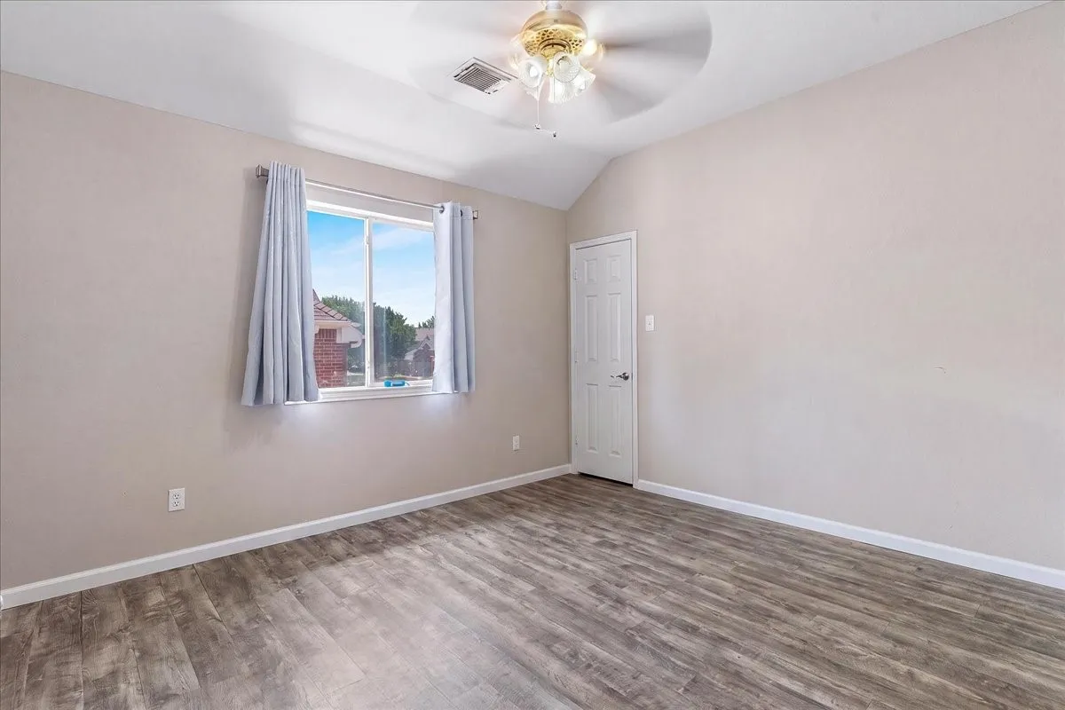 Spacious room featuring wood-finish flooring, a vaulted ceiling, and a ceiling fan with integrated lighting