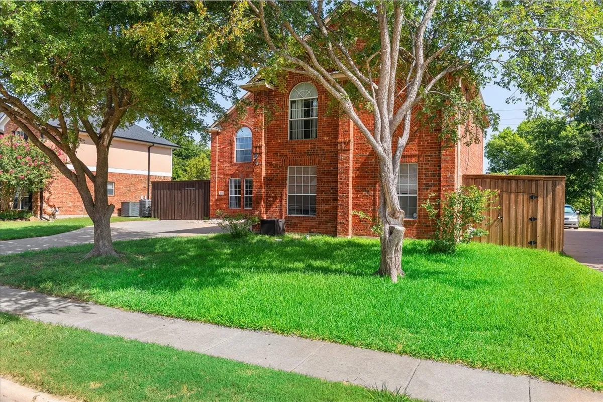 Red brick exterior featuring arched and rectangular window designs, a paved driveway, mature trees, and a wooden privacy fence