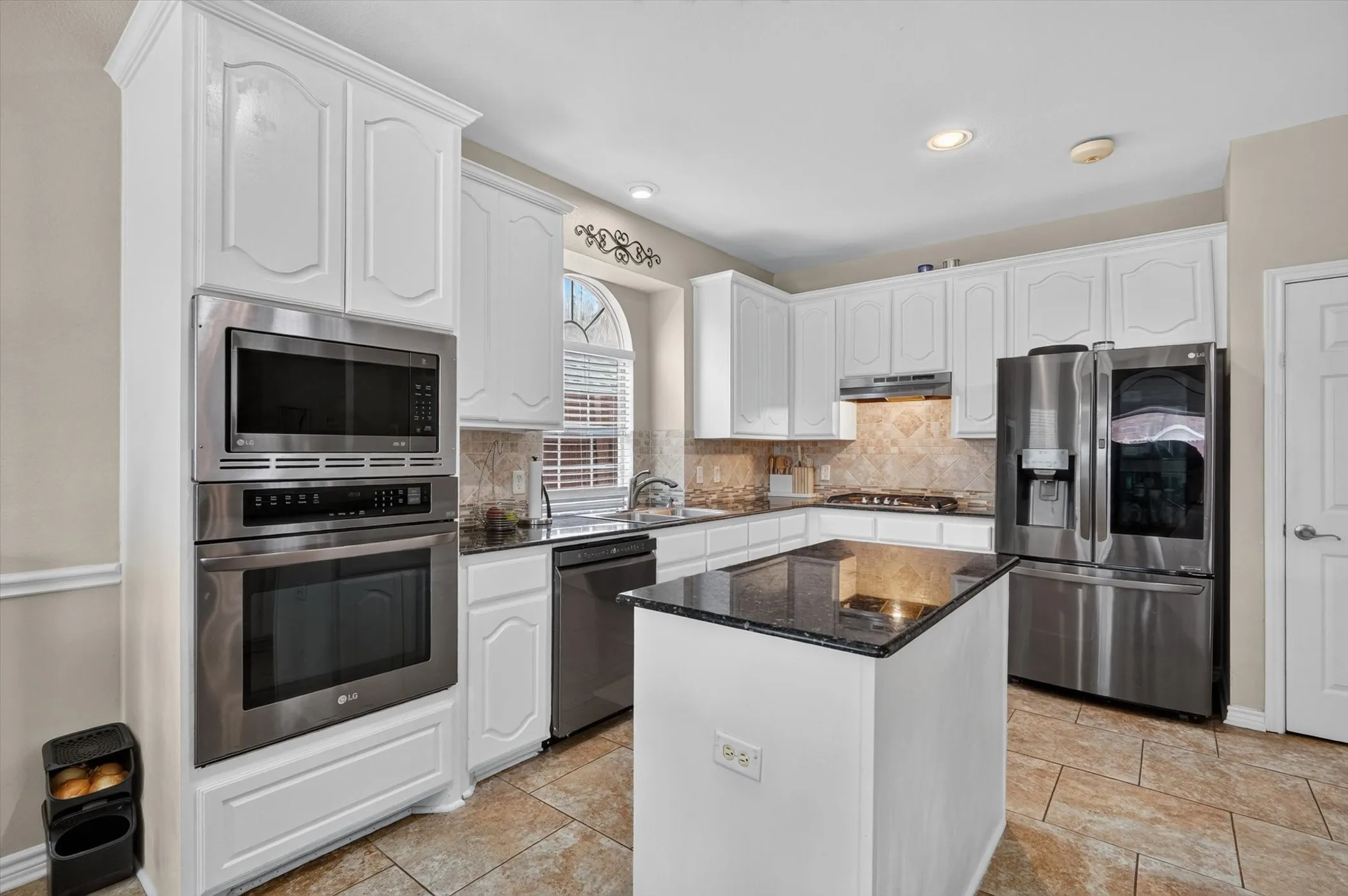 Kitchen featuring white cabinetry, built-in stainless steel appliances, dark stone countertops, an island with a stone surface, and tiled flooring