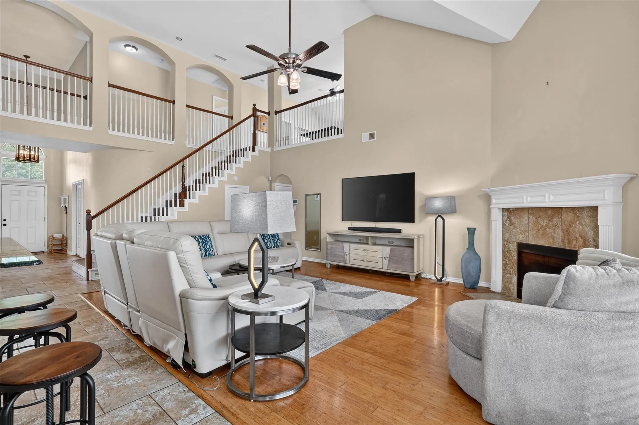 Two-story living area featuring wood-finish flooring, a tile-surround fireplace with a white mantel, and an open staircase with white balusters and a wood handrail