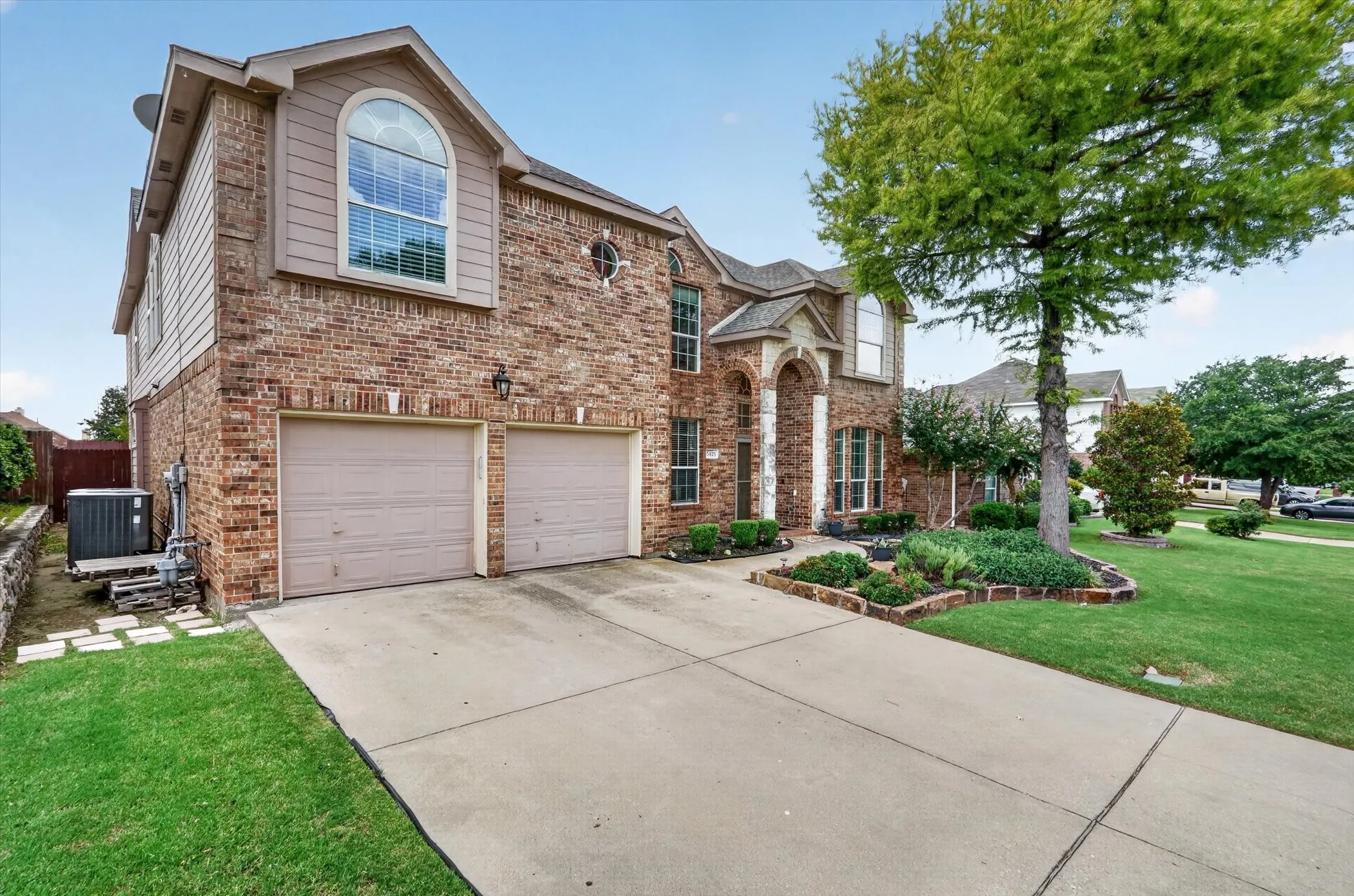 Brick and siding exterior featuring a two-car garage, arched entry, and a prominent arched window on the upper level