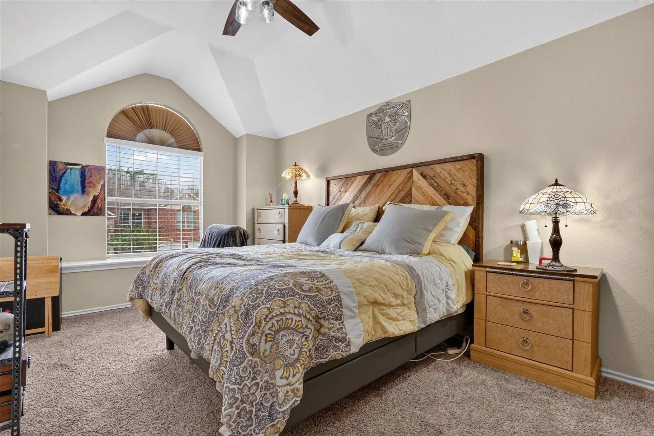 Vaulted ceiling bedroom featuring a large arched window with horizontal blinds, neutral wall tones, and carpet flooring