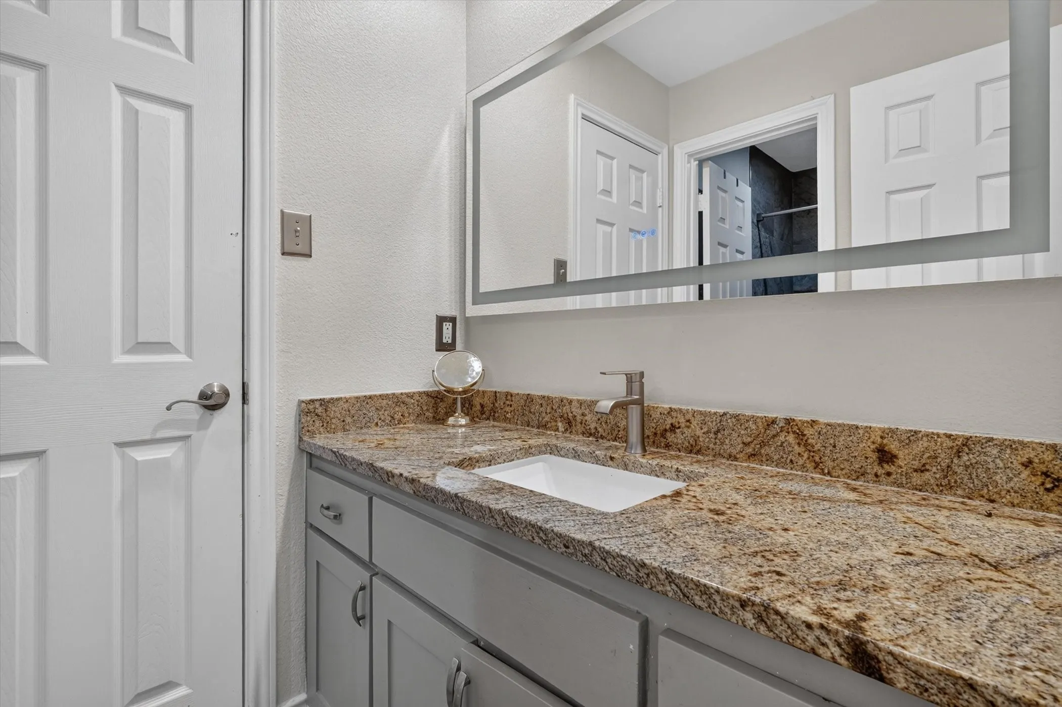 Bathroom vanity featuring a granite countertop with integrated sink, brushed nickel faucet, and gray cabinetry