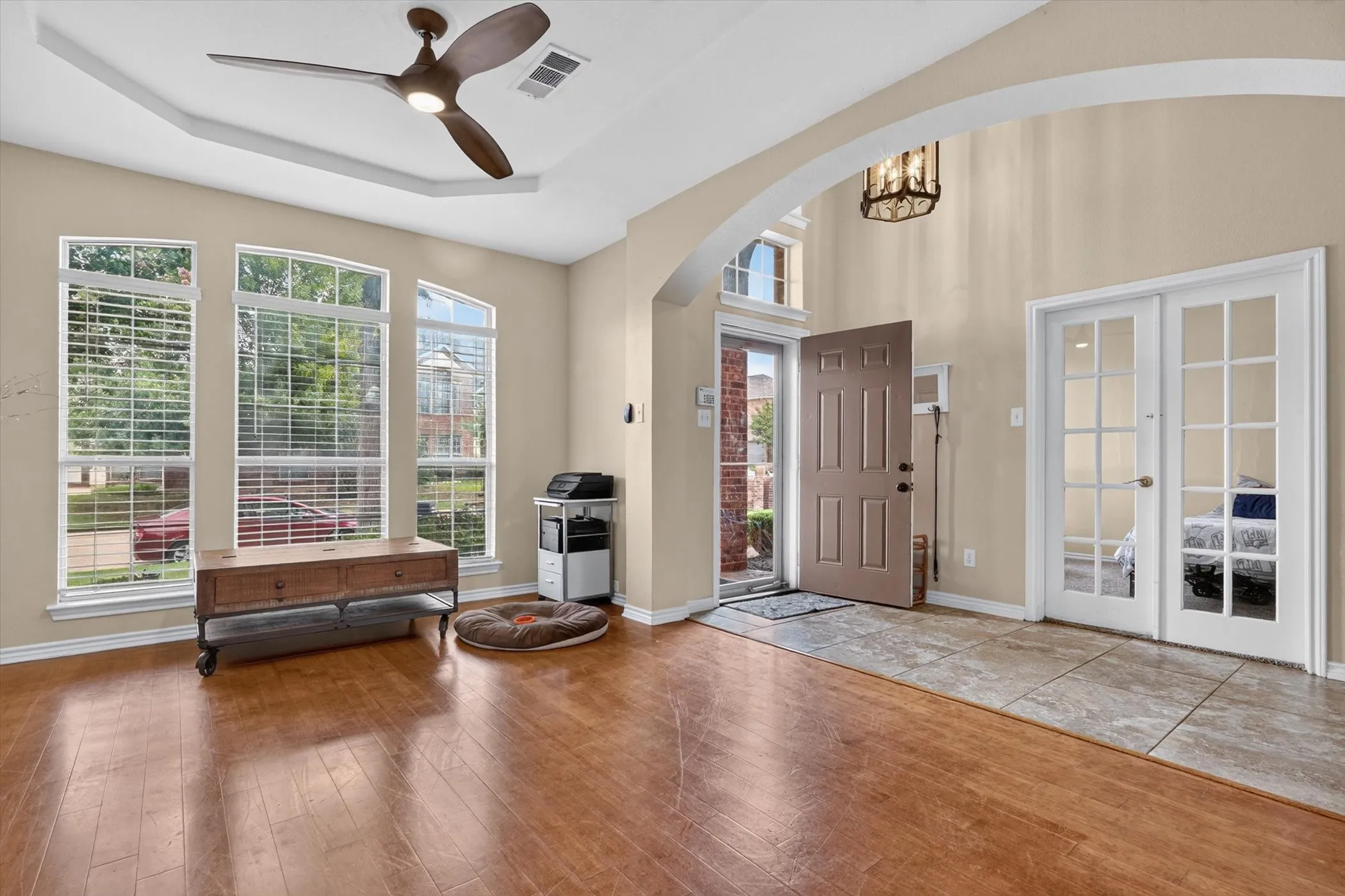 Foyer and living area featuring high ceilings, wood-finish flooring, a contemporary ceiling fan, three large windows with blinds, and double glass-paneled doors