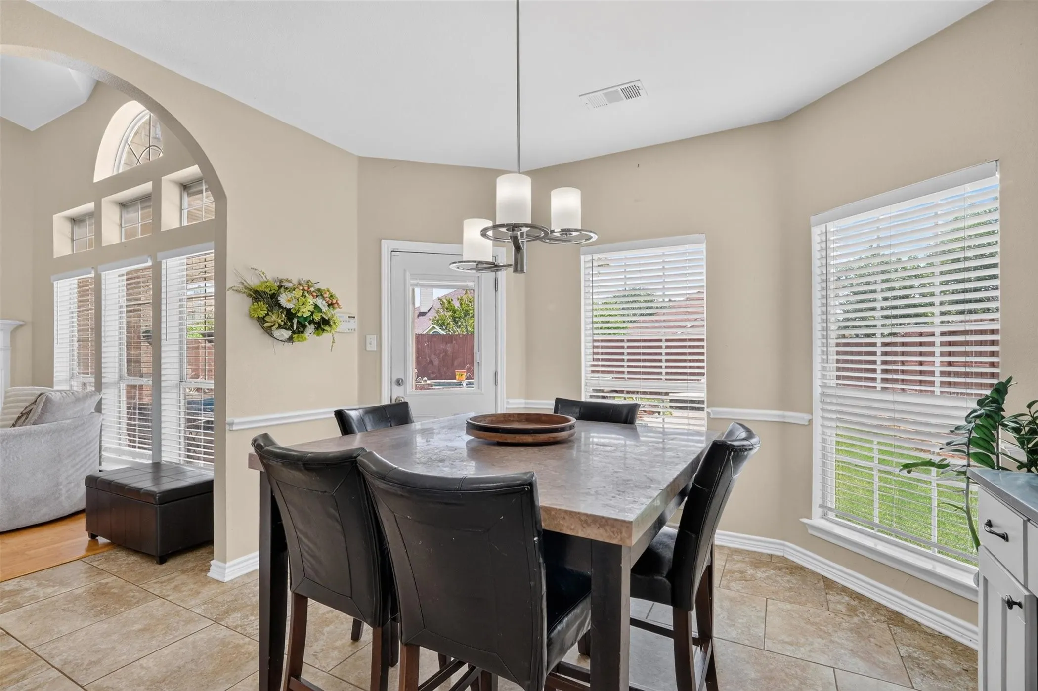 Dining area featuring ceramic tile flooring, a contemporary chandelier, multiple windows with blinds, a direct exterior door, and an arched architectural opening to an adjacent room