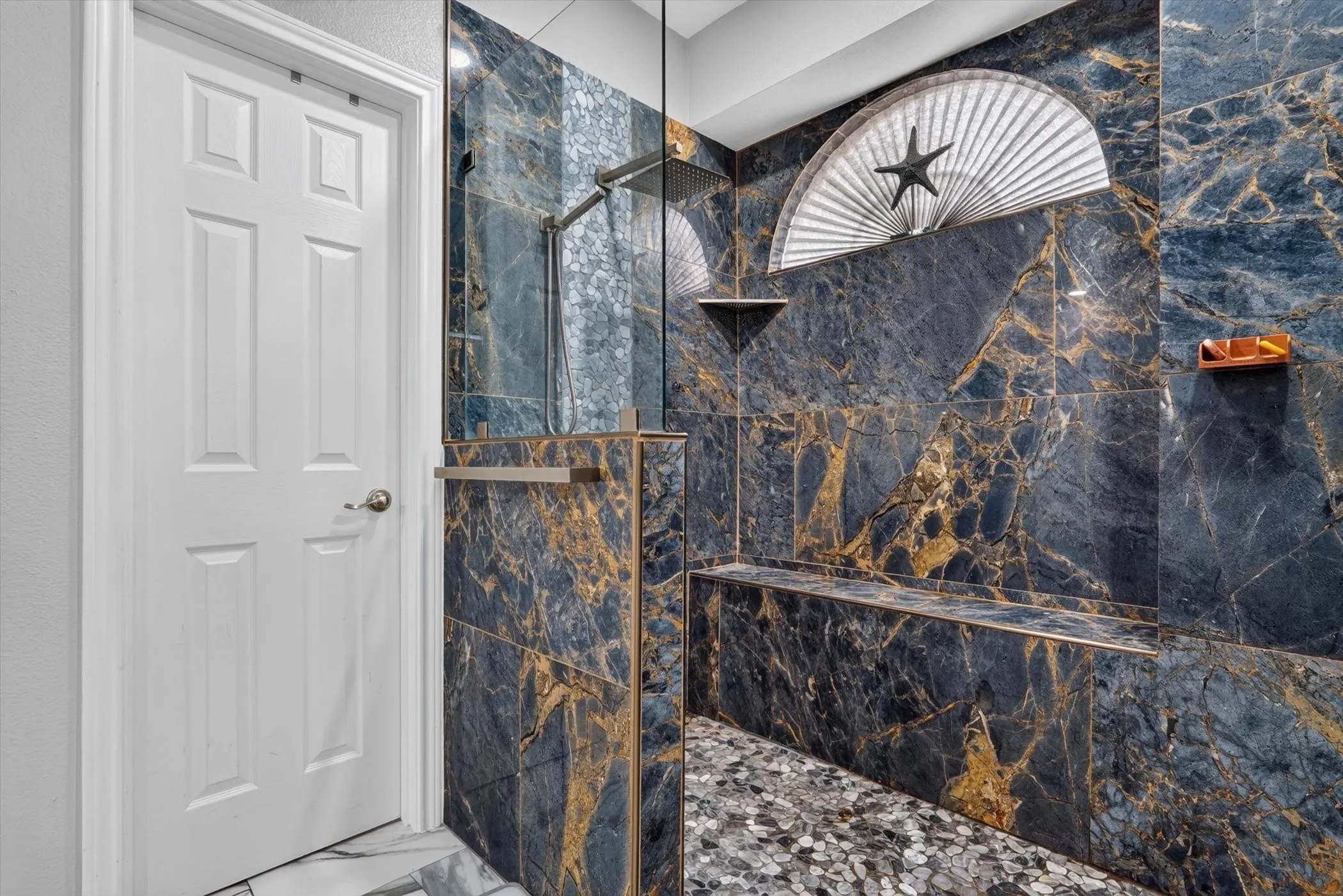 Shower enclosure with dark marbled tile walls, a built-in bench, and pebble-style flooring