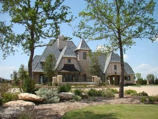 Stone exterior with turret details, a slate-style roof, an arched entry, and mature landscaping