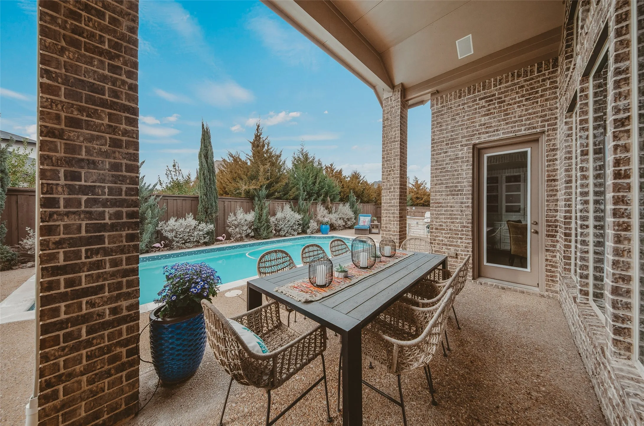 Covered outdoor patio area featuring a swimming pool, brick columns, a privacy fence, and a glass-paneled door