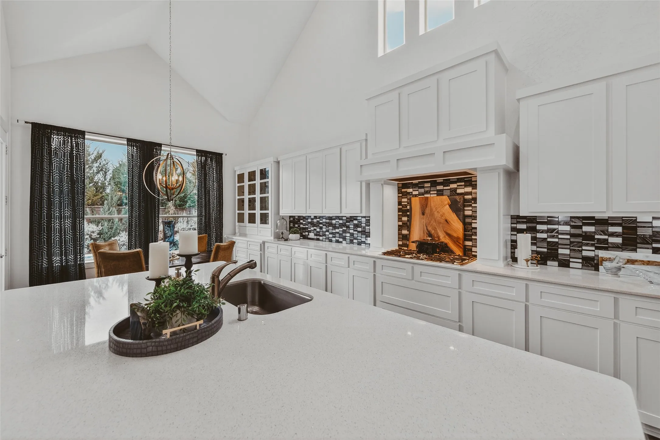 Expansive kitchen featuring a large island with an undermount sink, white cabinetry, and a mosaic tile backsplash