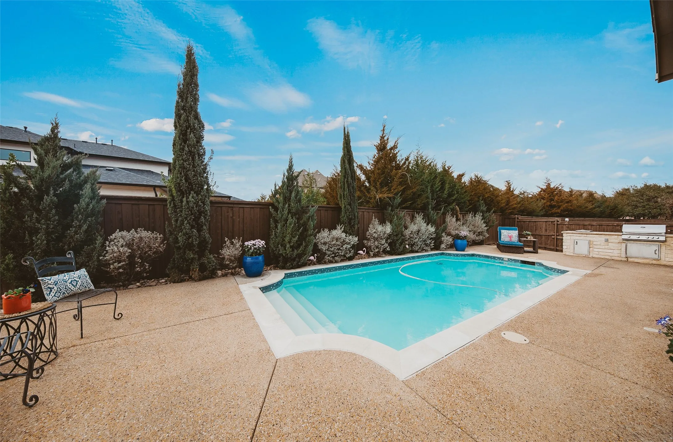 Swimming pool featuring integrated steps, exposed aggregate patio, and privacy fencing