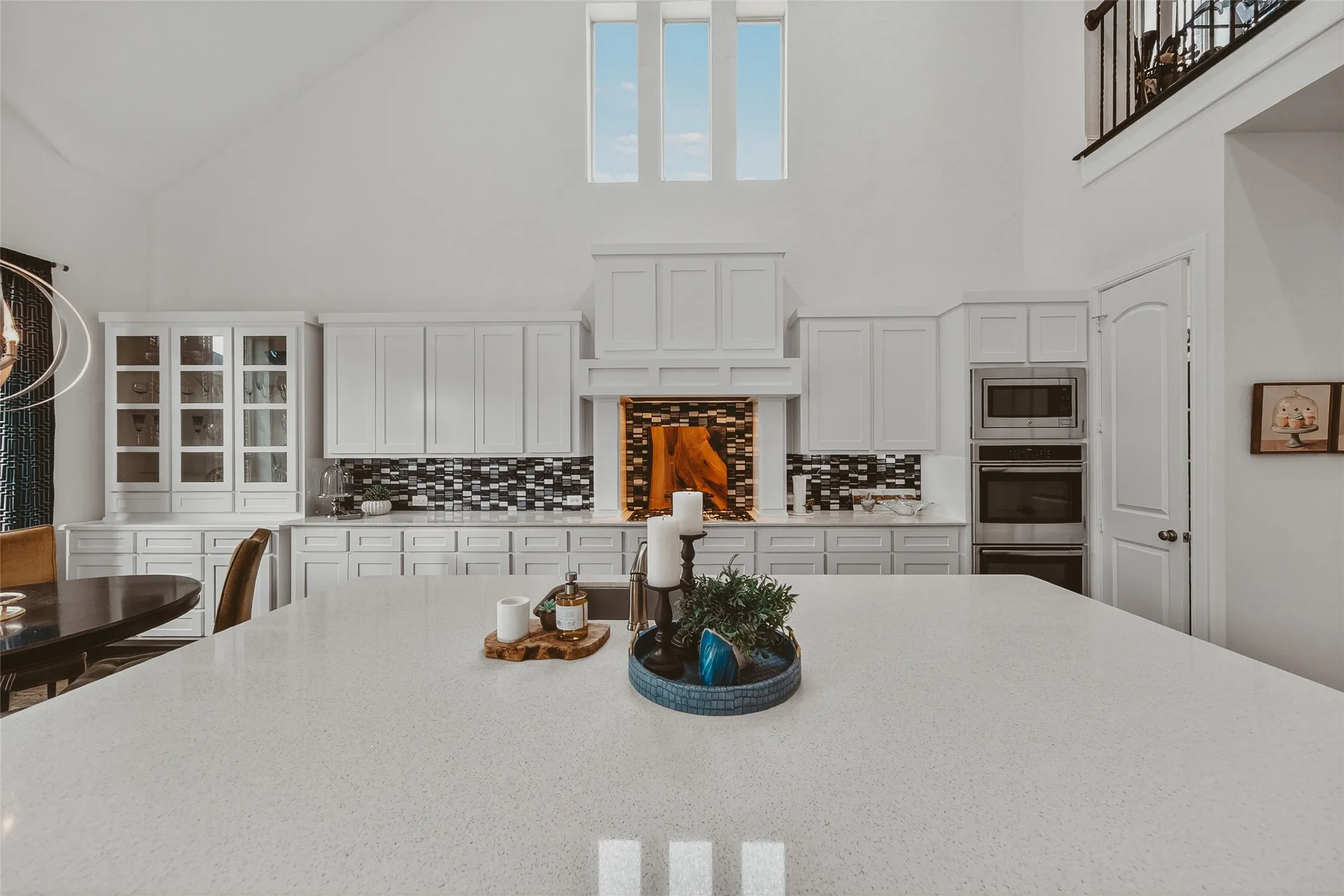 Spacious kitchen featuring a large central island with a light-toned countertop, white cabinetry with varied door styles, built-in stainless steel appliances, and a unique backsplash with decorative accents