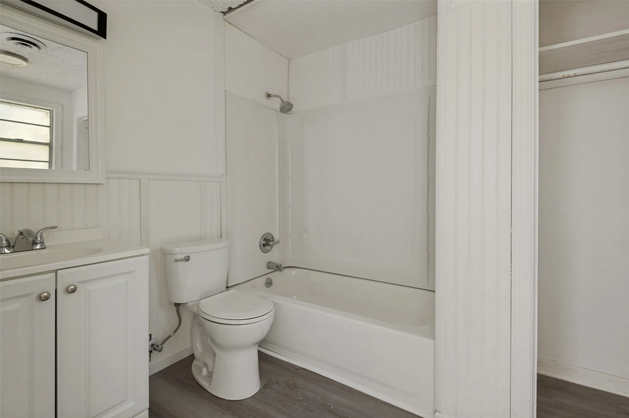 Bathroom featuring a vanity with a white countertop and chrome faucet, a white toilet, a white bathtub with a shower, and wood-finish flooring