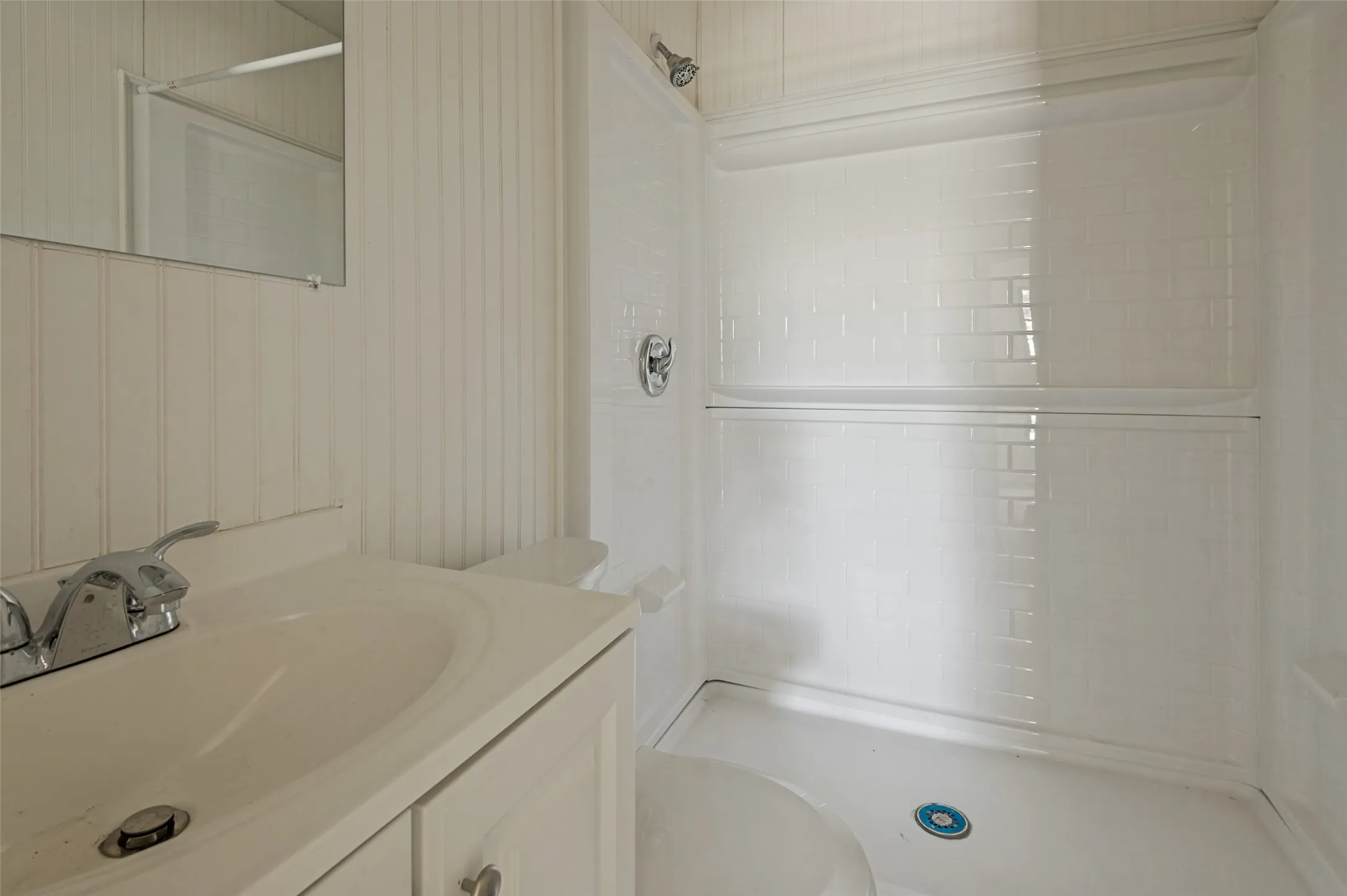 Bathroom featuring a white vanity with integrated sink, chrome faucet, and white beadboard paneling