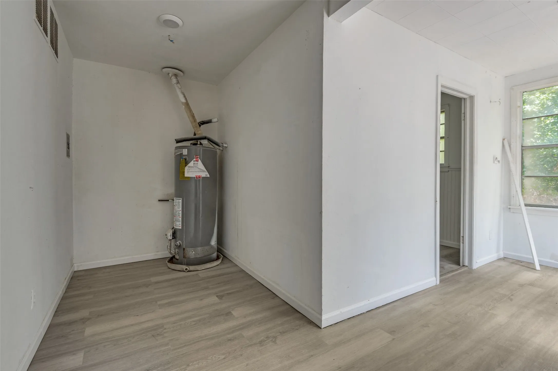 Utility room featuring a water heater, light wood-finish flooring, and white baseboards