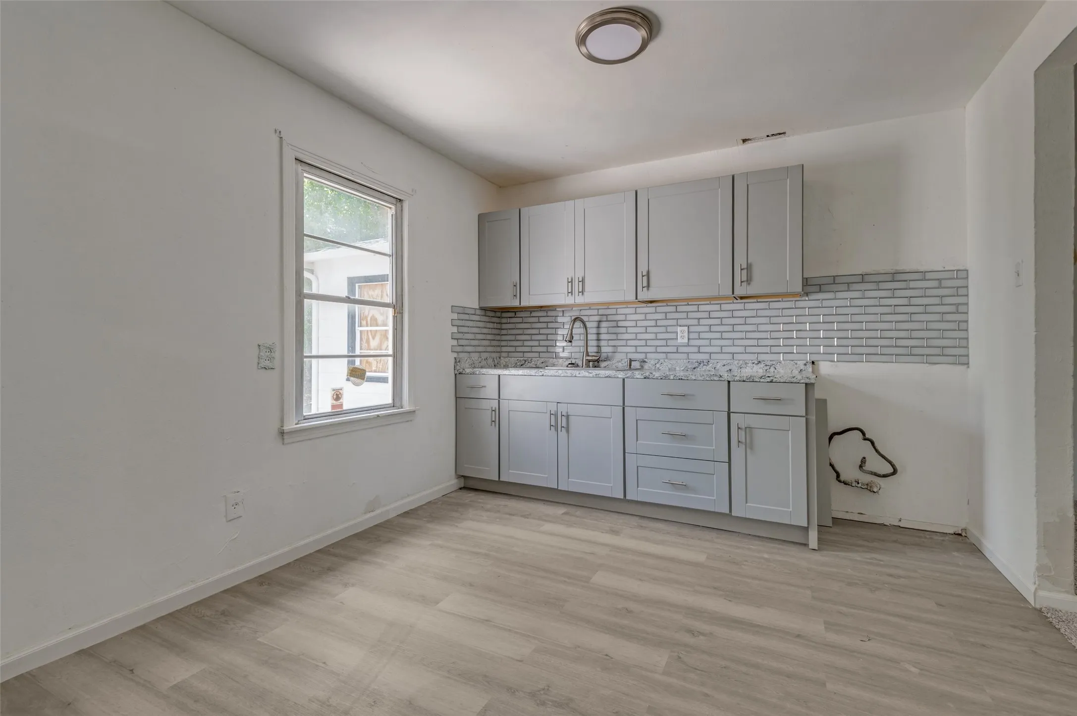 Kitchen area featuring light gray cabinetry, a white subway tile backsplash, a stainless steel sink with a gooseneck faucet, and light wood-finish flooring