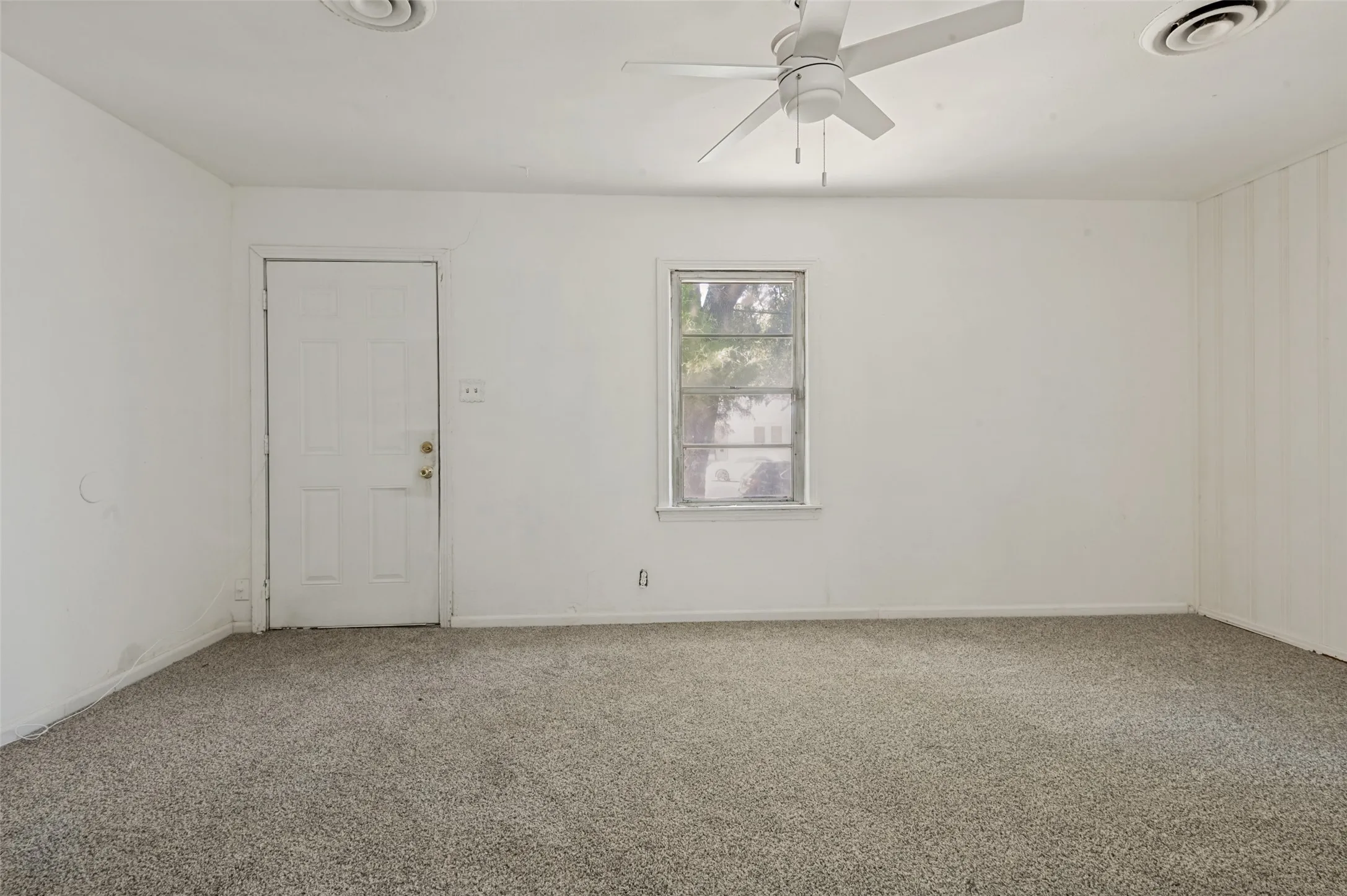 Carpeted room featuring a ceiling fan with light fixture, a window, a white paneled door, and recessed ceiling vents