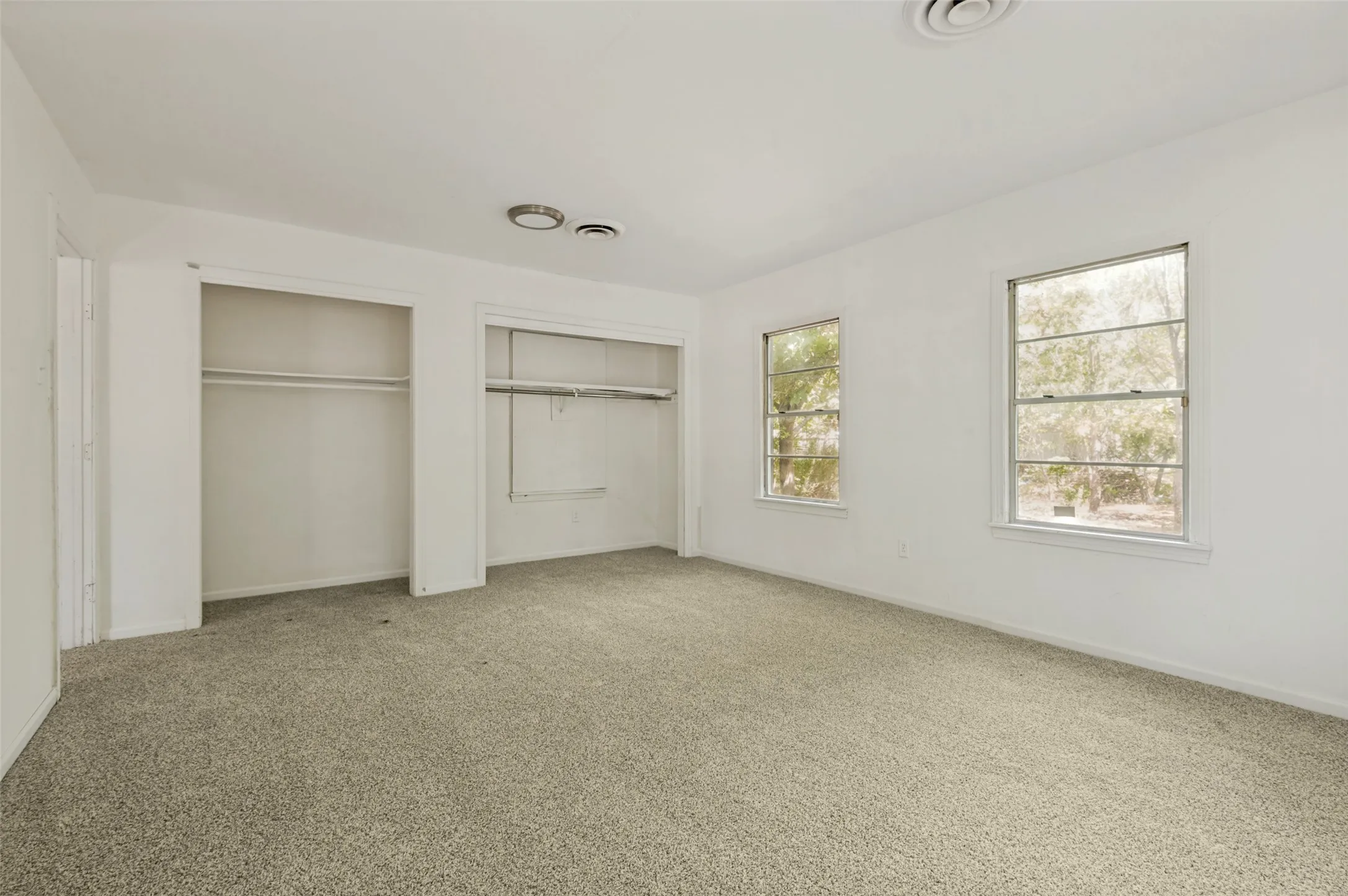Carpeted interior room featuring two large windows, dual built-in closets with hanging rods, and a ceiling-mounted light fixture