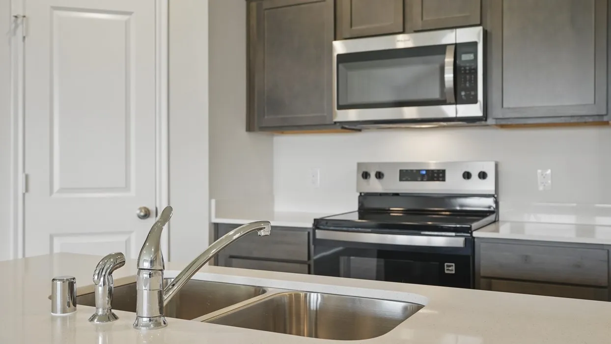 Kitchen featuring a double basin stainless steel sink with a high-arc faucet, light-toned countertops, gray cabinetry, a built-in microwave, and an electric range with a glass cooktop