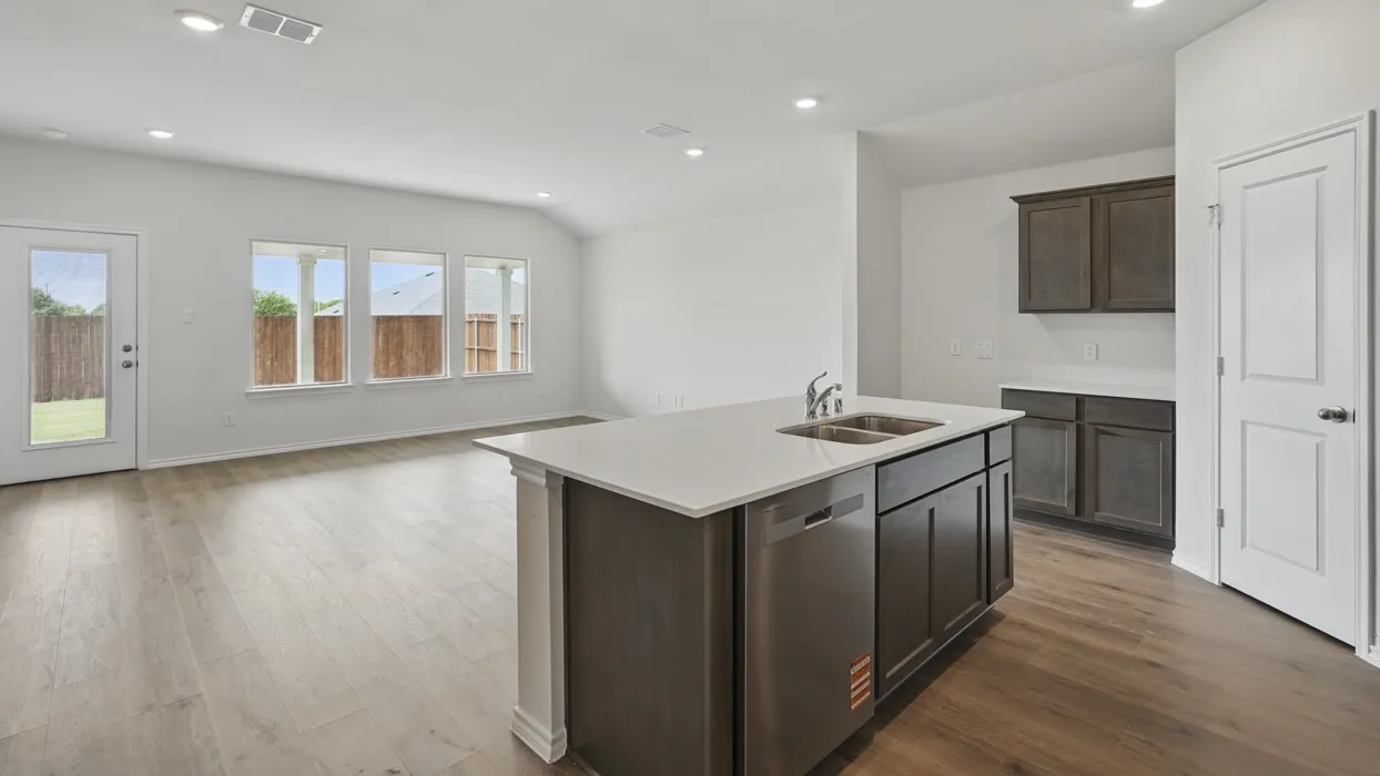Open-concept living area featuring wood-finish flooring, a kitchen island with integrated sink and dishwasher, recessed lighting, and multiple windows
