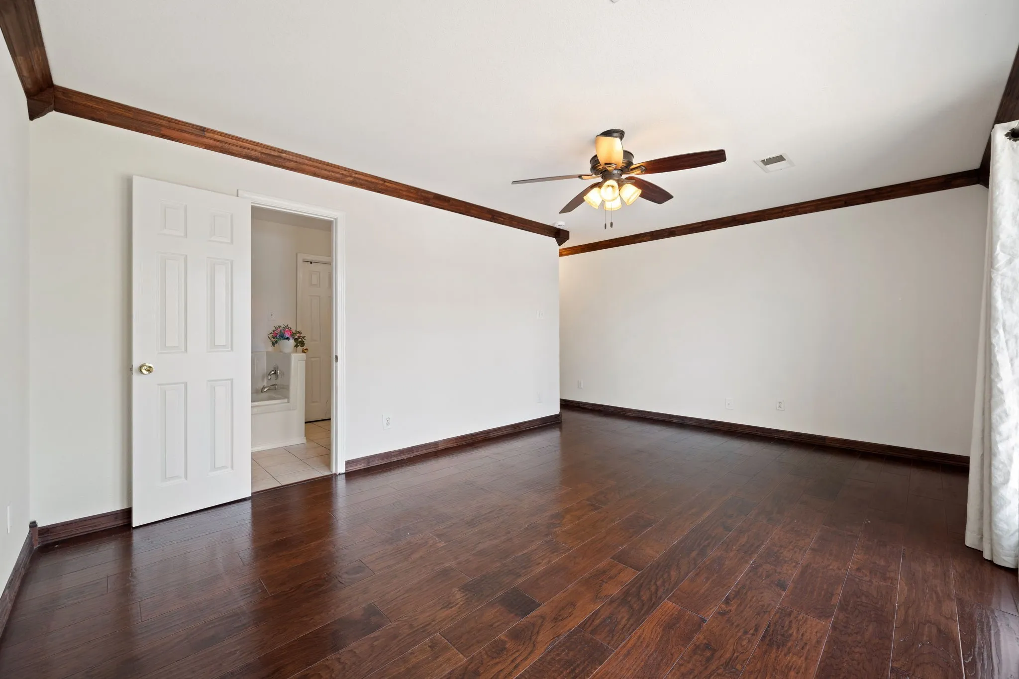 Spacious Primary room featuring wood-finish flooring, white walls, and dark wood trim