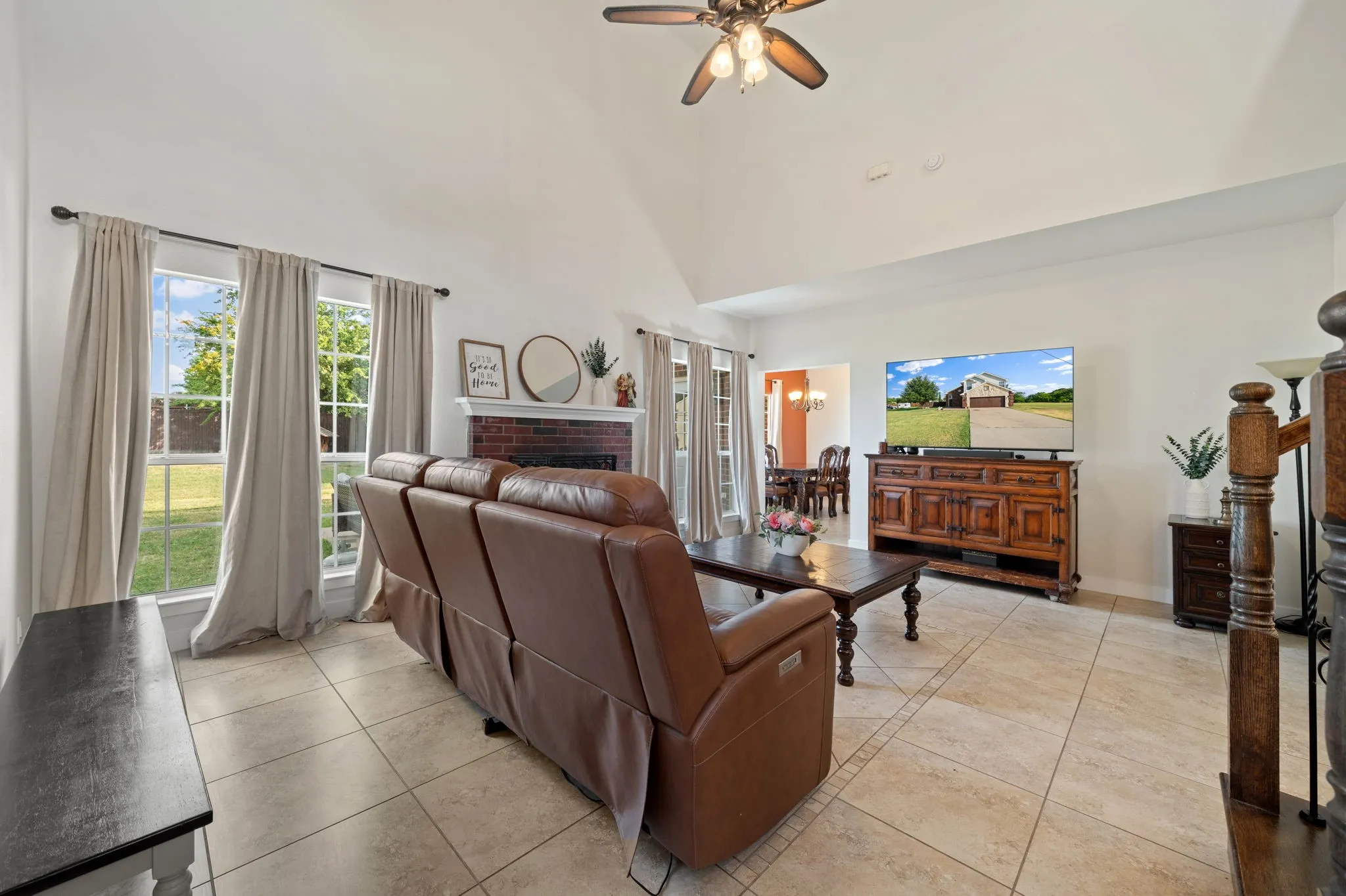 Vaulted ceiling living area featuring a brick fireplace, light-toned tile flooring, and multiple windows providing natural light