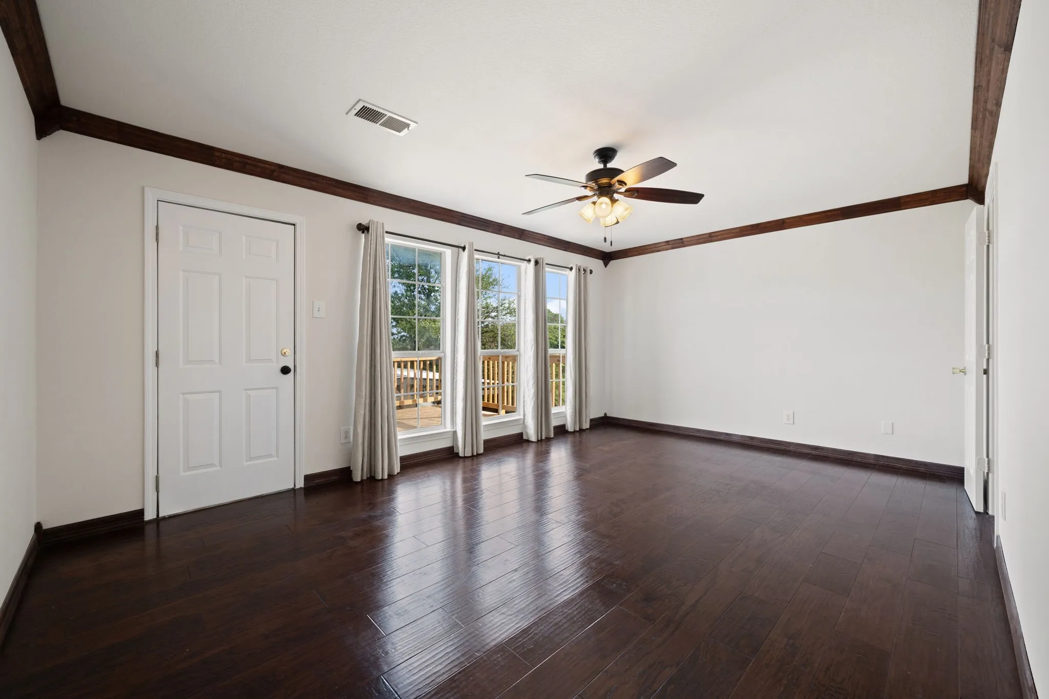 Spacious Primary room featuring dark wood-finish flooring, white walls, and decorative ceiling beams