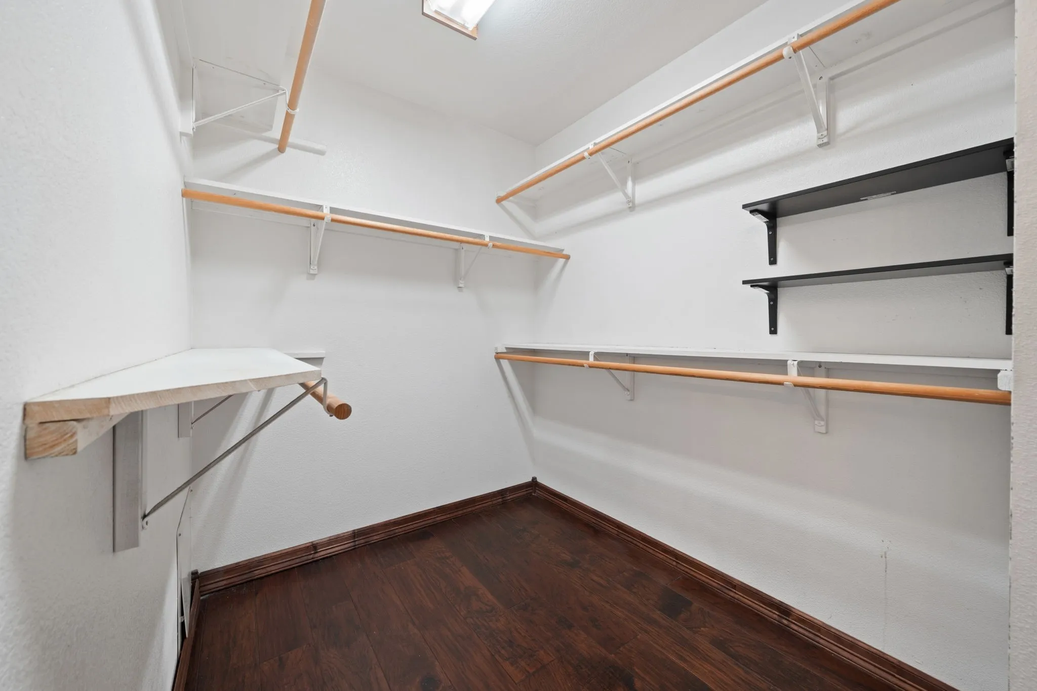 Spacious primary closet featuring dark wood-finish flooring, white walls, and built-in shelving