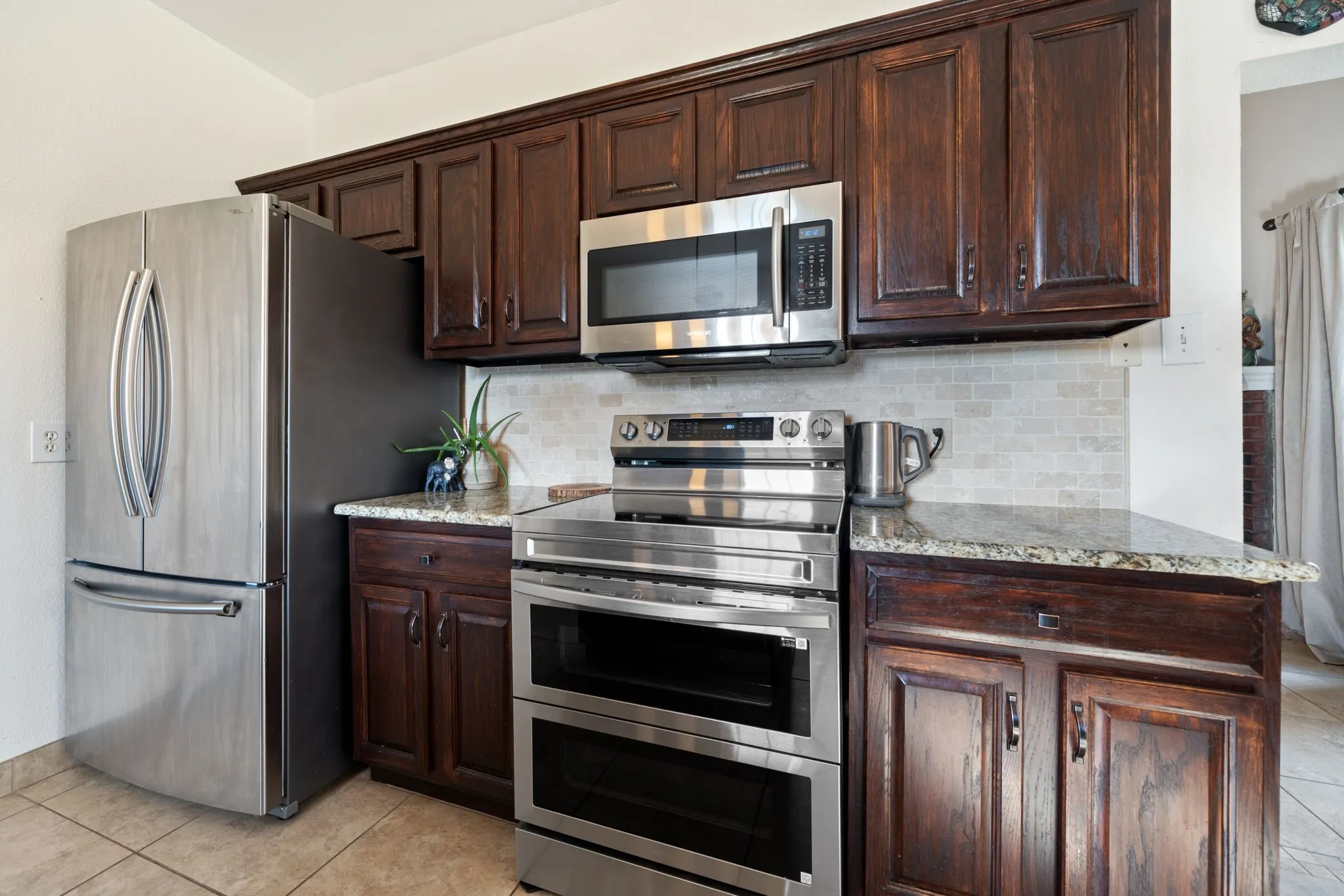 Kitchen featuring wood cabinetry, light-toned tile backsplash, and stone countertops