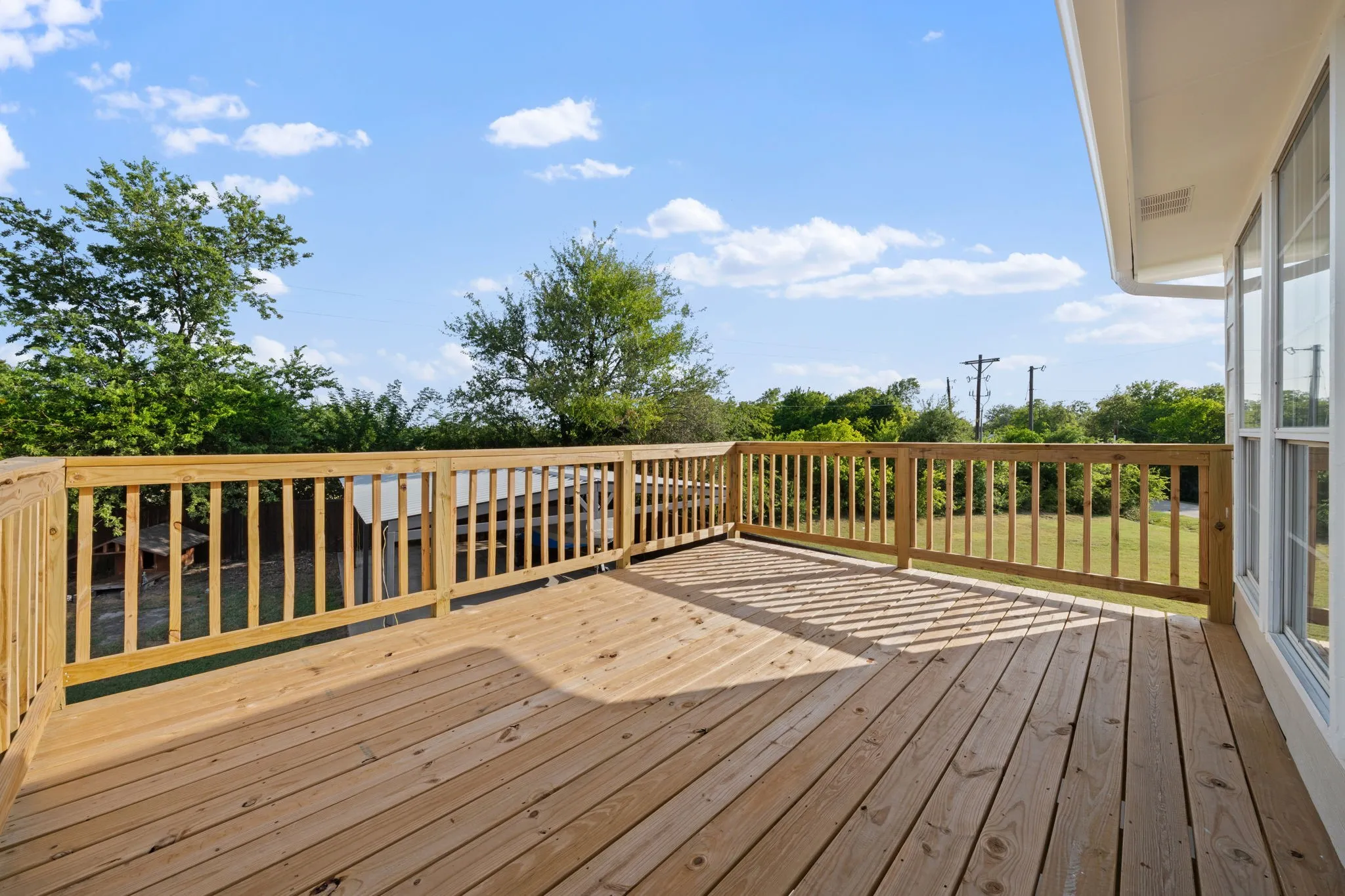 Expansive wood deck with natural finish, featuring a surrounding wood railing, and a windowed exterior wall