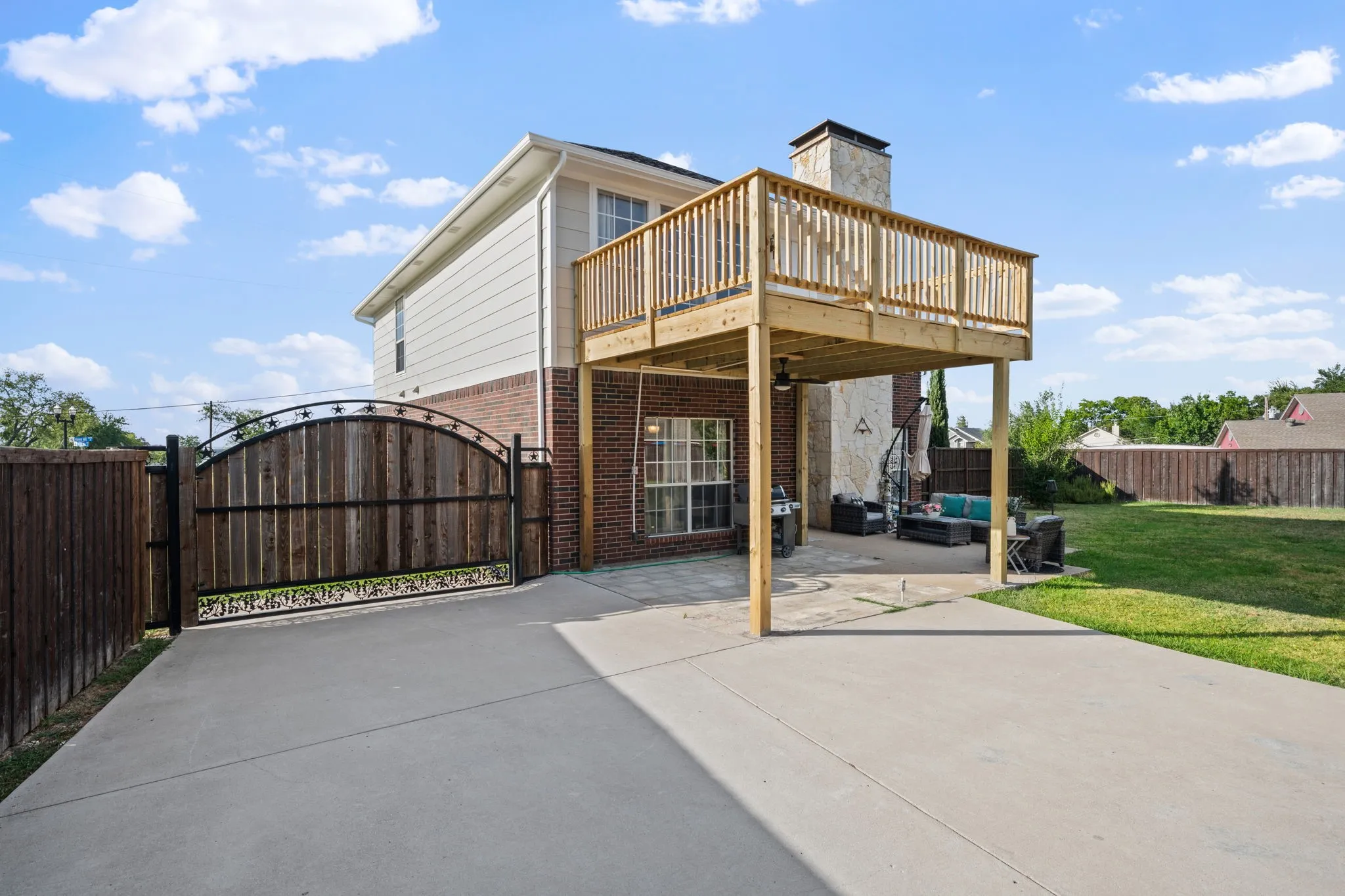Two-story exterior featuring brick and siding finishes, a second-story wood deck, and an expansive concrete driveway