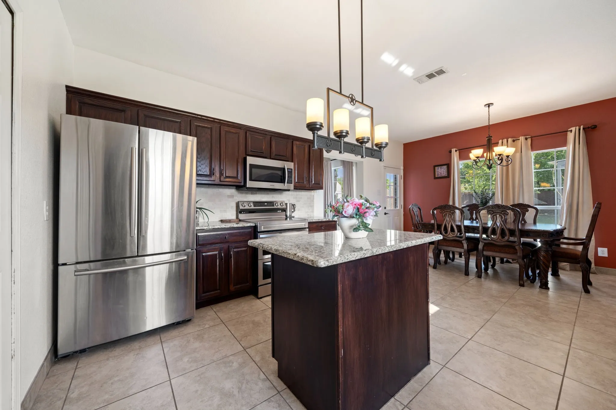 Kitchen and dining area featuring dark wood cabinetry, stainless steel appliances, a granite-topped island, tile flooring, and a chandelier lighting fixture