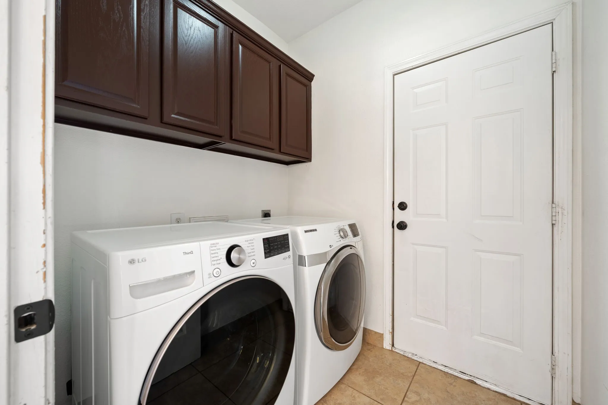 Laundry area featuring dark wood-finish cabinetry, neutral wall paint, and ceramic tile flooring