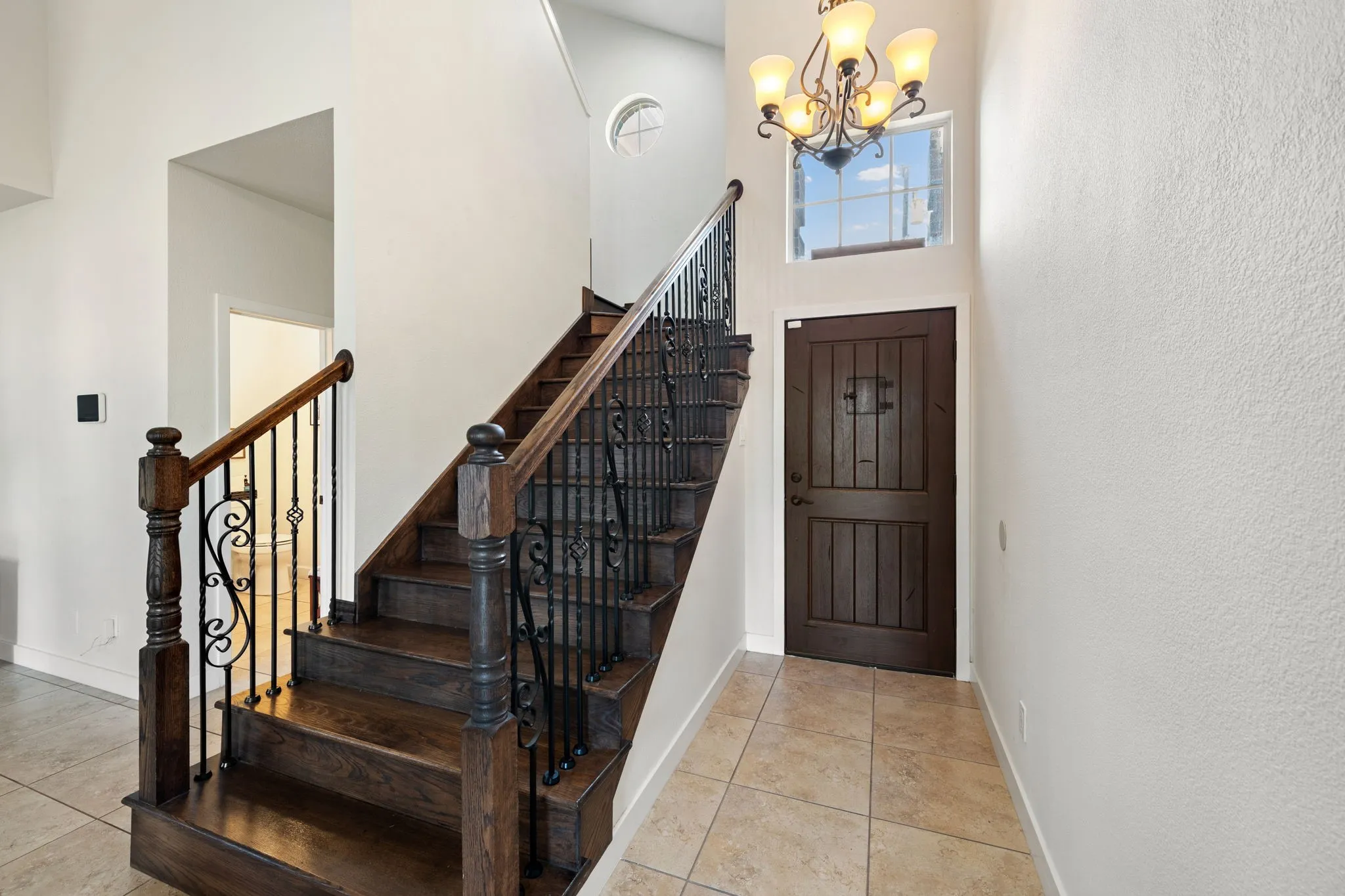 Grand entry foyer featuring a dark wood staircase with wrought iron balusters, a solid wood entry door, and large format tile flooring